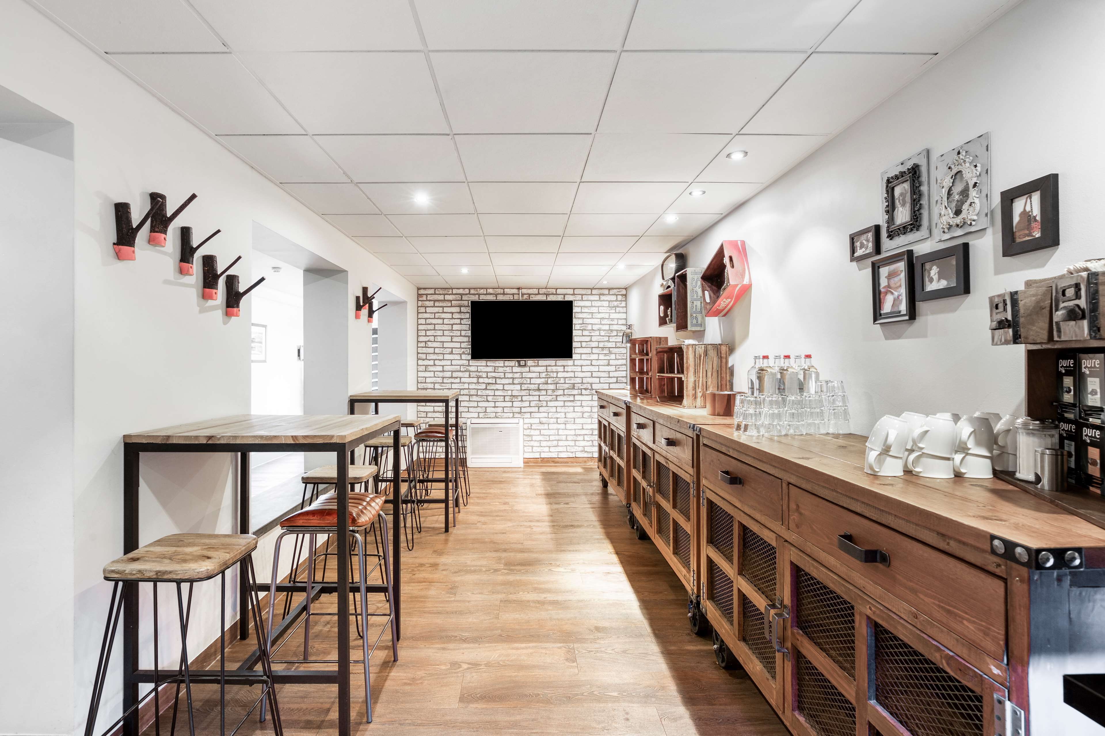 Un espace bar moderne avec un long comptoir, des tabourets et un mur en briques en arrière-plan.