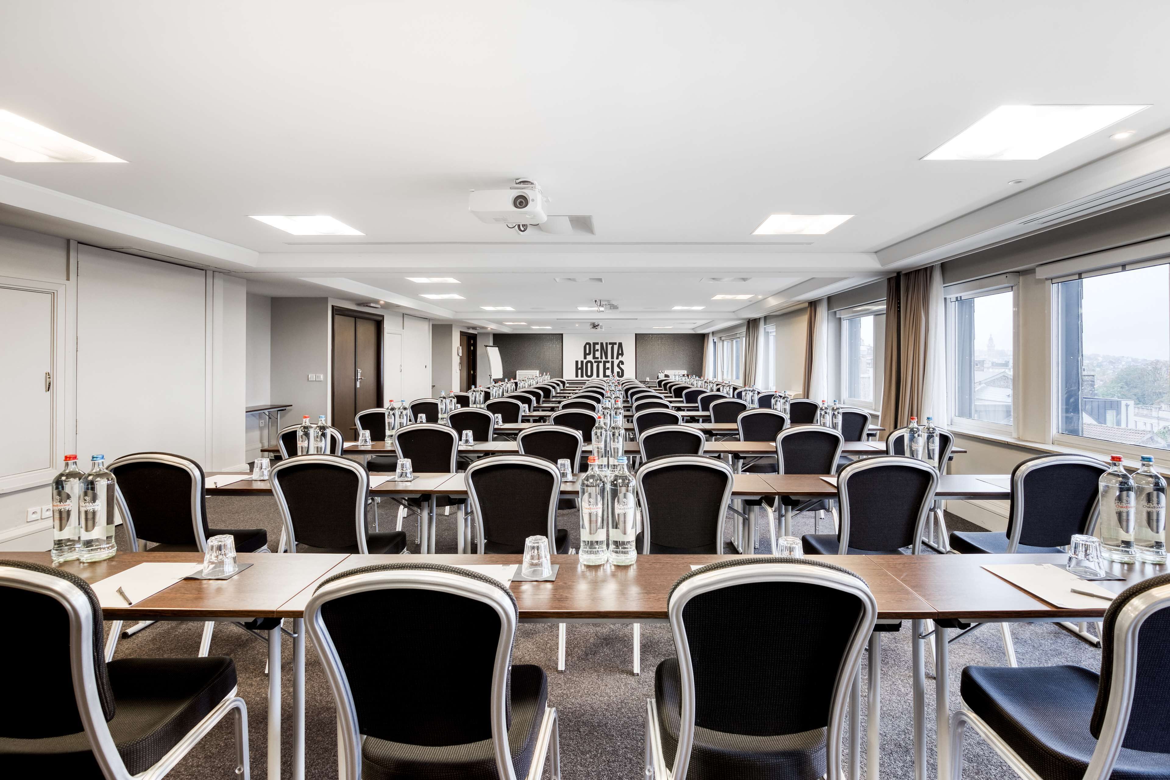 Un salón de conferencias con filas de mesas y sillas, botellas de agua y un cartel de Penta Hotels.