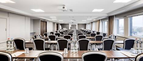 Un salón de conferencias con filas de mesas y sillas, botellas de agua y un cartel de Penta Hotels.