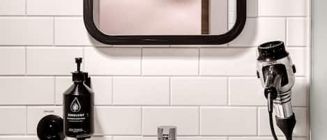 A bathroom with a white sink, a mirror, a hairdryer, and a bottle of Zenology shampoo.