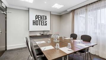A conference room with a large table, four chairs, and a projector screen displaying "PENTA HOTELS".