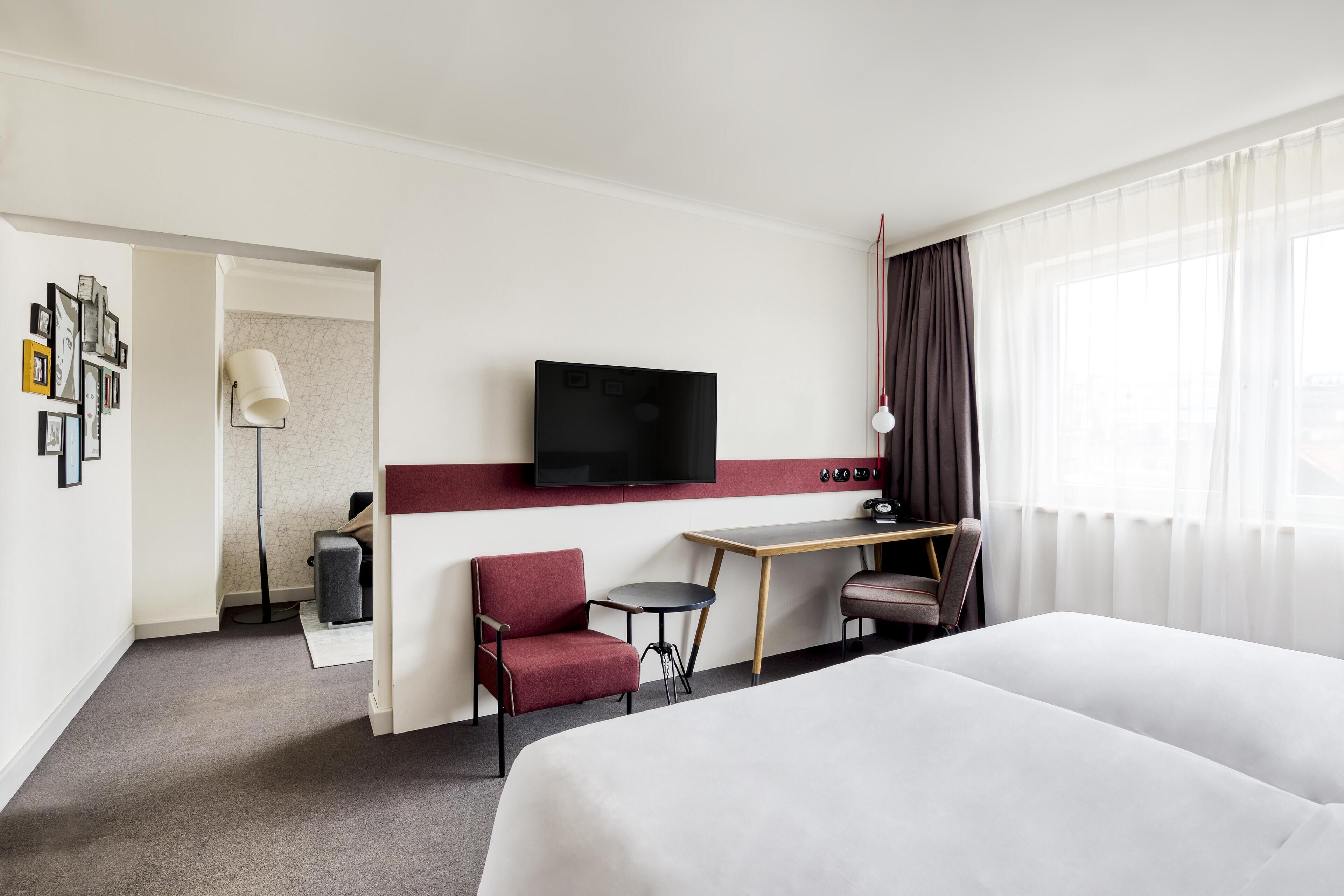 Een hotelkamer met een bed, een bureau, een stoel, een televisie en een raam met gordijnen.