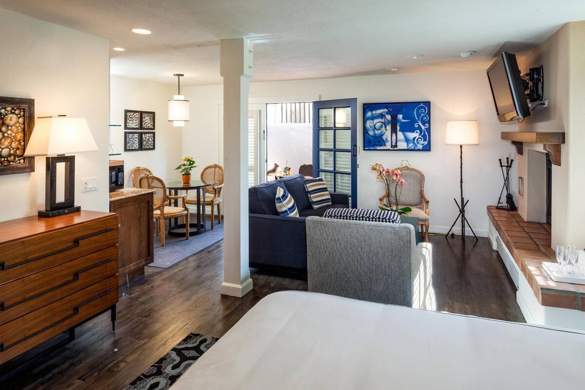 A modern hotel room with a bed, a sofa, a desk, and a dining area. There are chairs, a table, and a television.