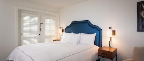 A hotel room with a large bed, two bedside tables, a chair, and a door with white blinds.