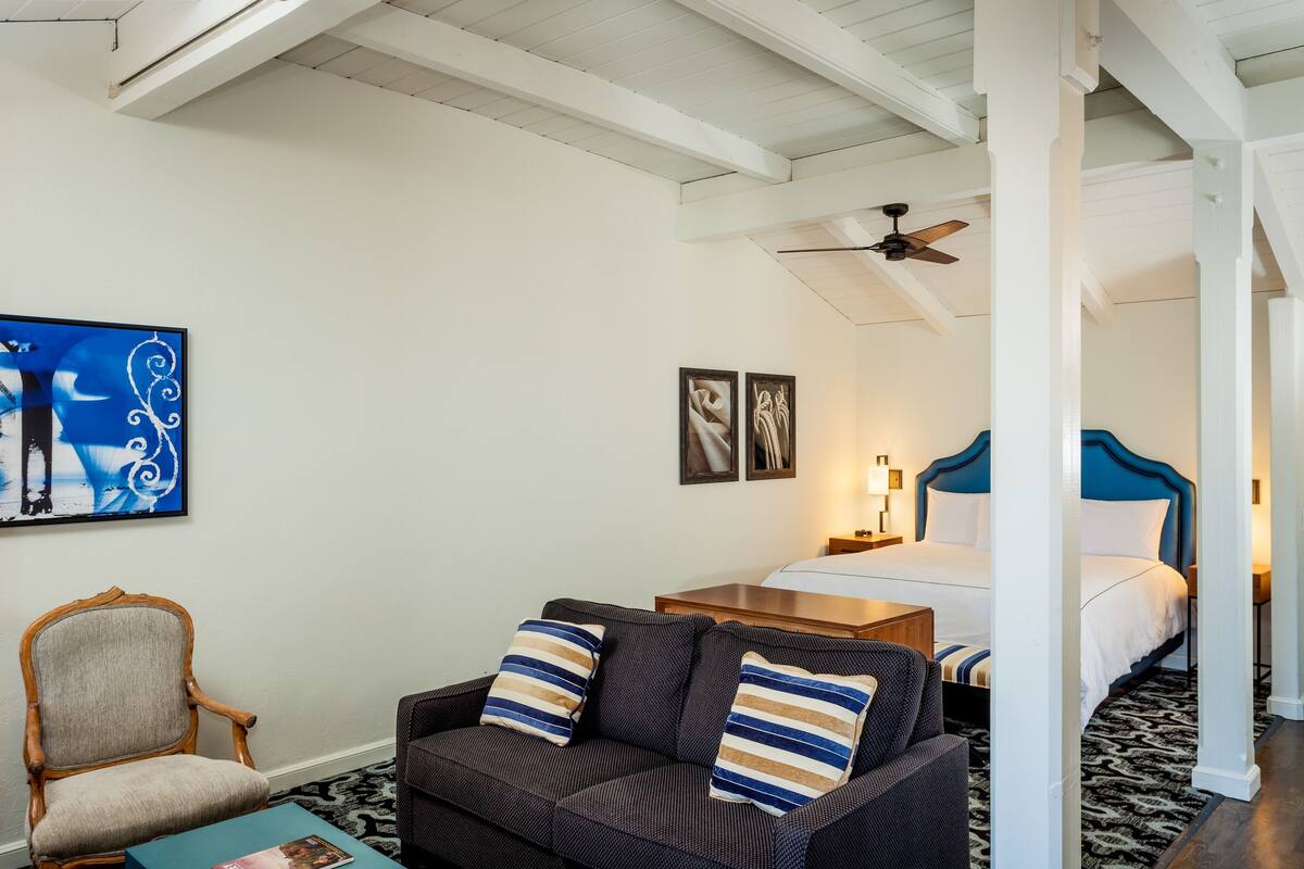A hotel room with a bed, a sofa, a chair, and artwork on the walls.