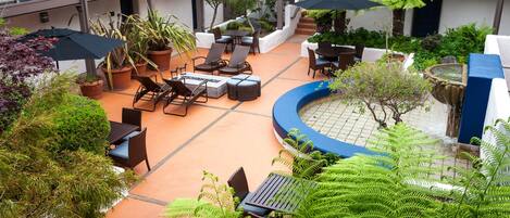 Un patio con mesas al aire libre, plantas en macetas y una fuente.