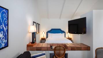 Una camera d'albergo con un letto, una televisione a parete, una scrivania con una sedia e un quadro incorniciato.