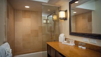 Un baño moderno con ducha envuelta en vidrio, tocador con artículos de aseo y un espejo grande.