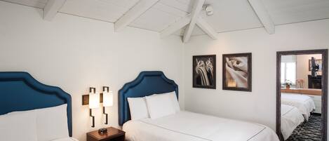 Une chambre d’hôtel avec deux lits, du linge de lit blanc, une tête de lit en bois, une table de chevet avec une lampe et un grand miroir.
