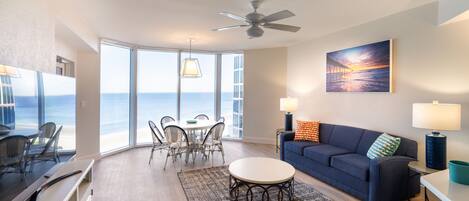 A modern living room with a blue sofa, a round coffee table, and a dining area with chairs and a table.