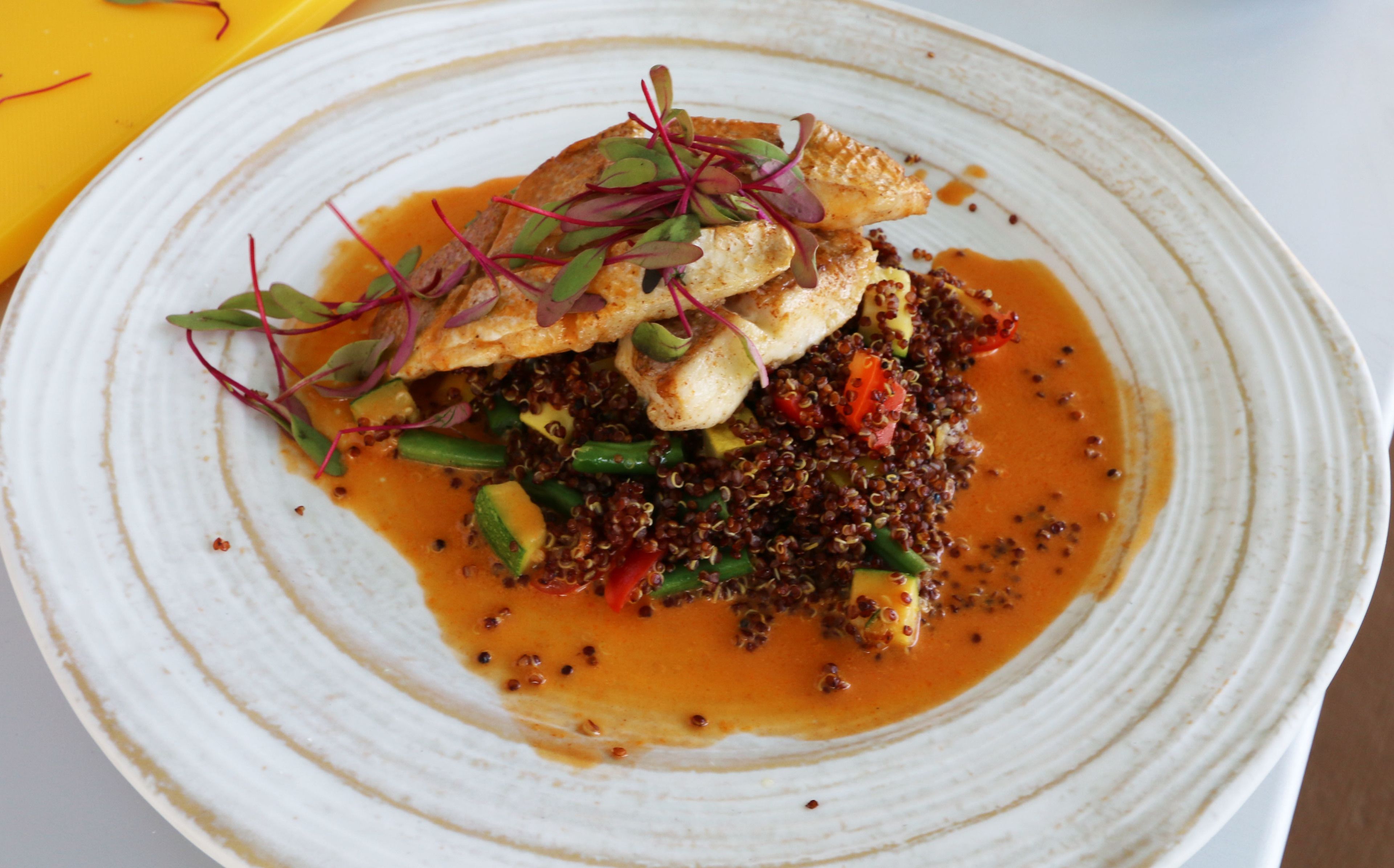 A plate of food with quinoa, vegetables, and fish, served on a white plate.