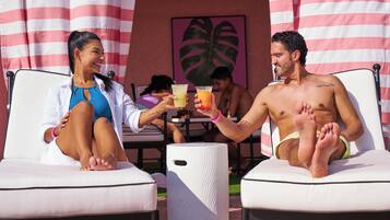 Two people sitting on lounge chairs with drinks, a table, and a large plant in the background.