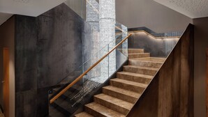 Een moderne trap met glazen balustrade, houten leuning en een gestructureerde wand.