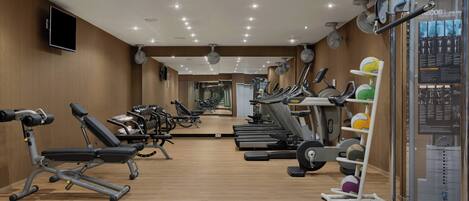 Un gimnasio con equipo de ejercicio, un televisor y un espejo grande.