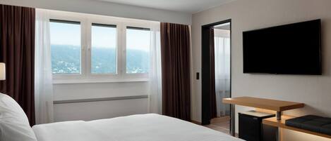 A hotel room with a large bed, a desk, a flat-screen TV, and a view of the mountains.
