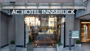 De ingang van AC Hotel Innsbruck met een moderne glazen gevel, grote deuren en een bord.
