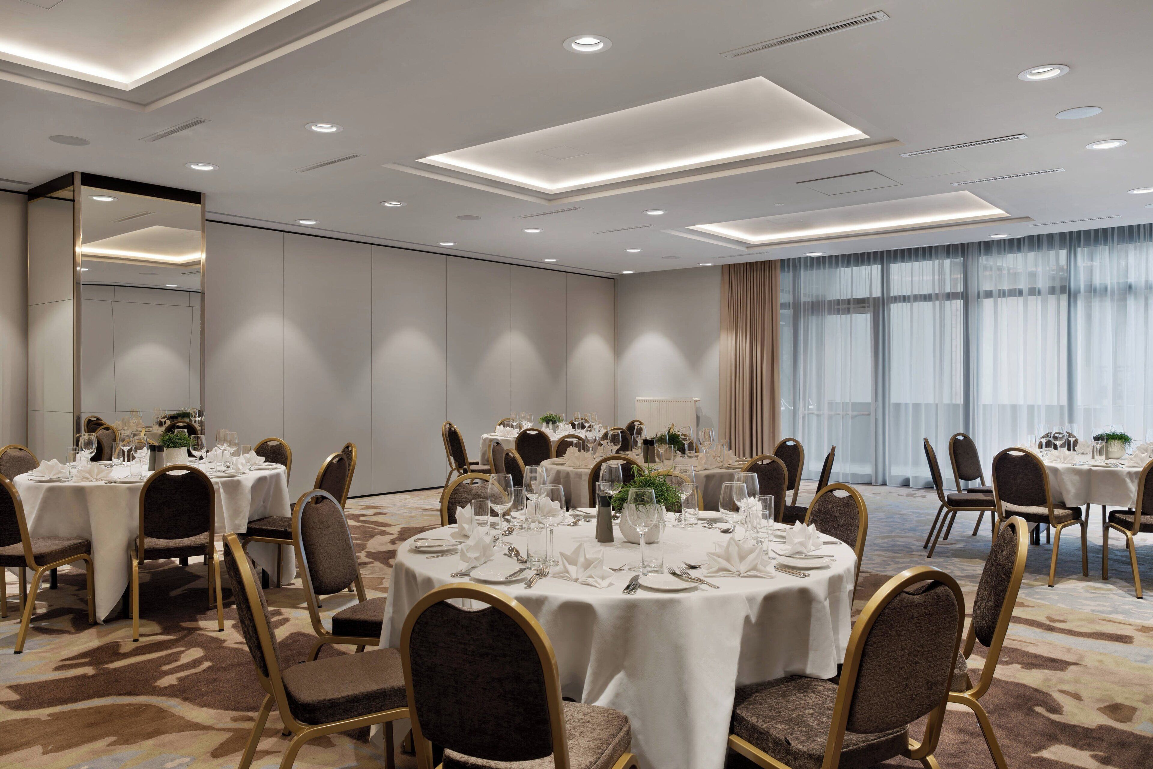 Un salón de conferencias con varias mesas redondas dispuestas para comidas, equipado con sillas y menaje de mesa.