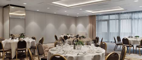 A conference room with multiple round tables set for dining, equipped with chairs and table settings.