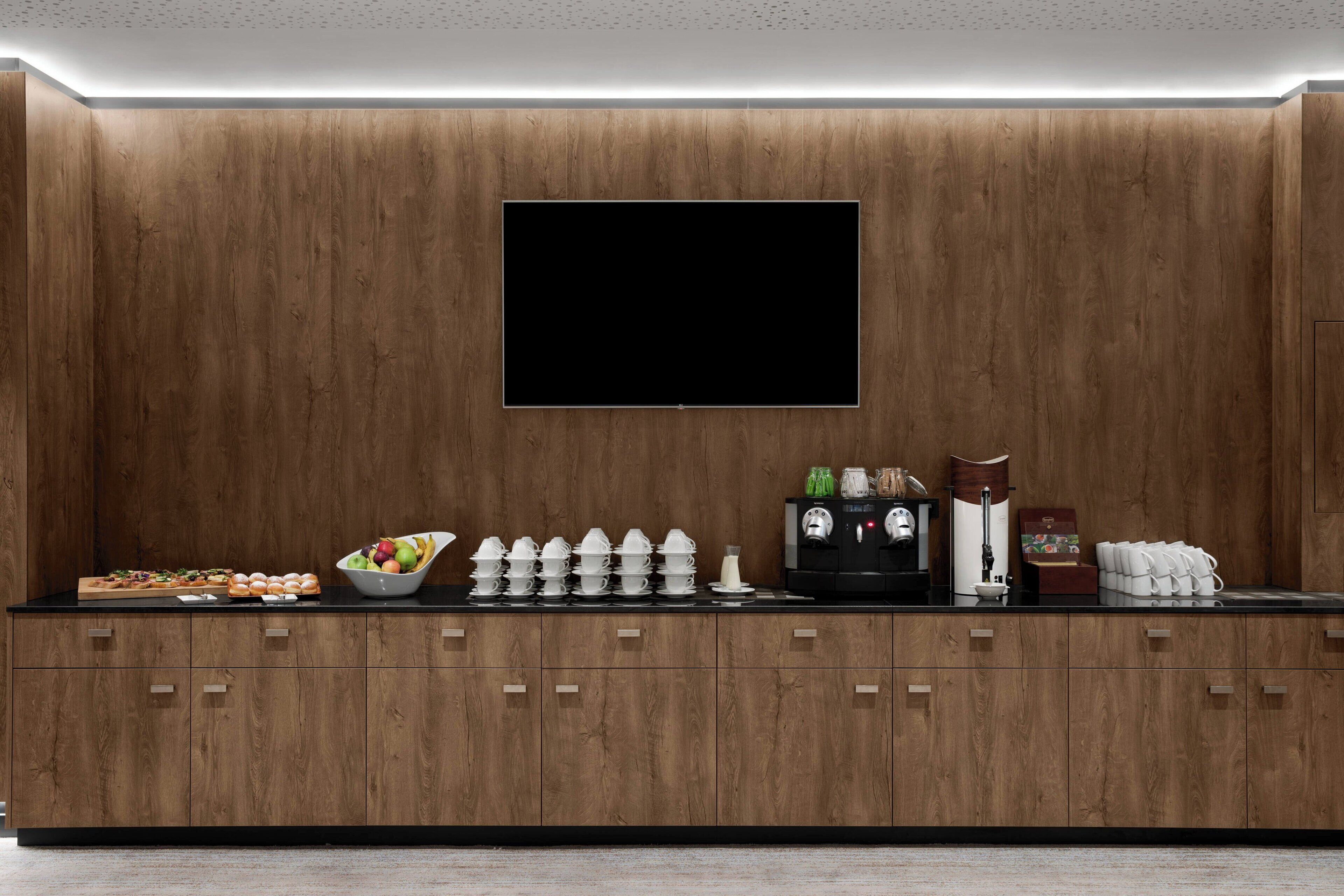 A modern kitchen with wooden cabinets, a flat-screen TV, and various kitchenware on the counter.