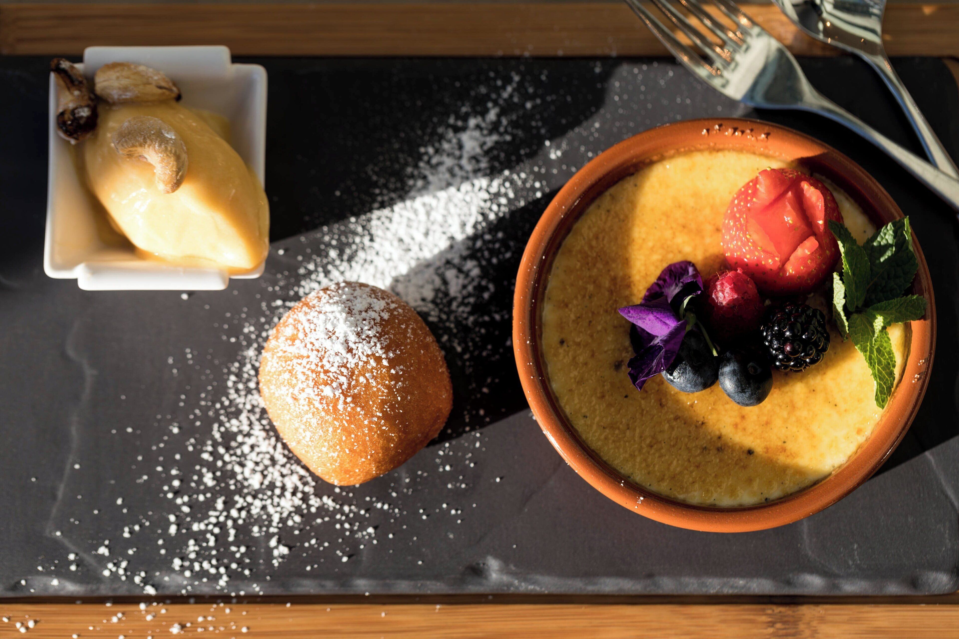 A dessert tray with a custard-like dish topped with berries and mint, a pastry with powdered sugar, and a small bowl of a similar dessert.