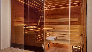 A sauna with wooden benches, a bench with towels, and a wooden bucket.