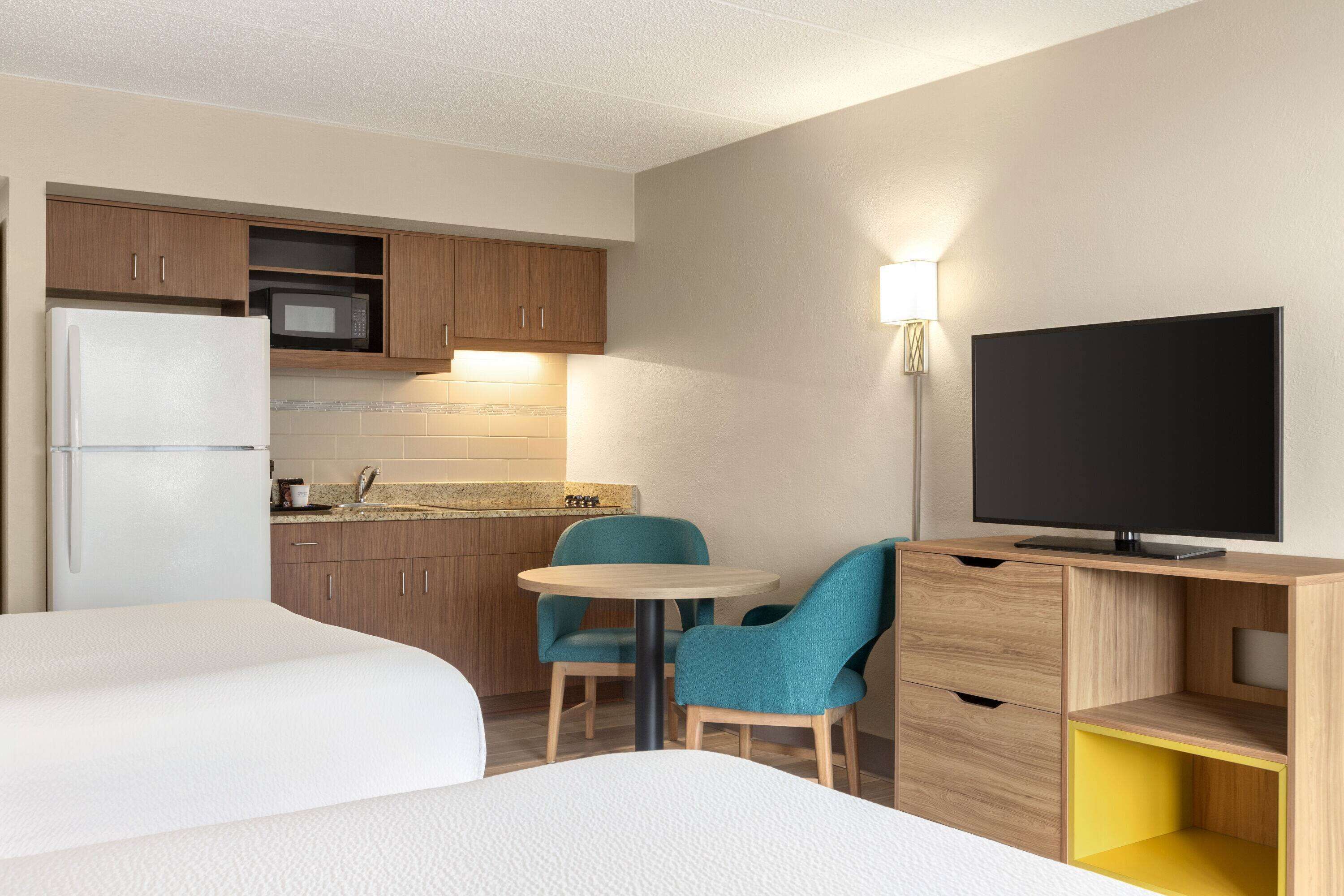 A hotel room with a bed, a small round table, two chairs, a TV, a microwave, and a refrigerator.