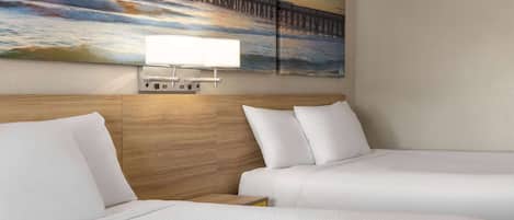 Habitación de hotel con dos camas, cabecera de madera, un cuadro de un muelle y una lámpara de pared.