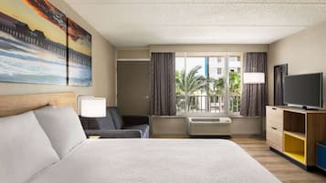 A hotel room with a large bed, a sofa, a TV, and a window with curtains.
