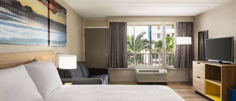 A hotel room with a large bed, a sofa, a TV, and a window with curtains.