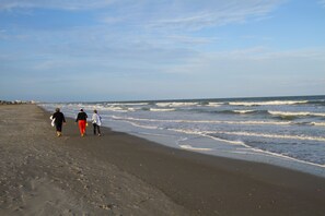 Ein Strand mit drei Personen, die am Ufer entlanggehen.