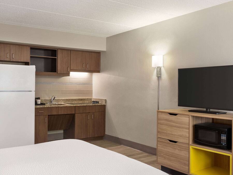 Une chambre d’hôtel de taille réduite, équipée d’une kitchenette, d’un lit, d’une télévision et d’un four à micro-ondes.