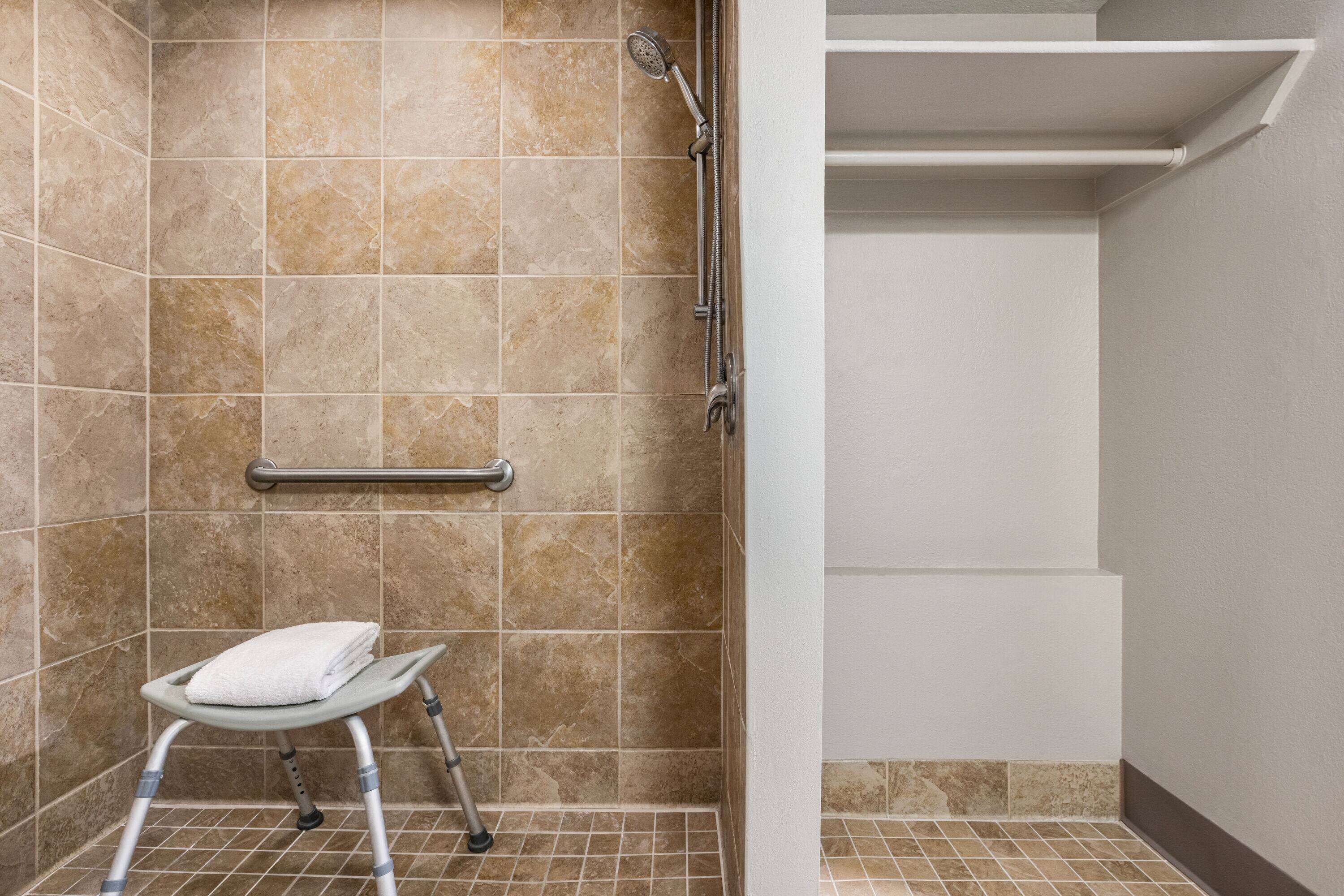 A bathroom with beige tiles, a shower, a grab bar, and a step stool.