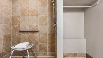 A bathroom with beige tiles, a shower, a grab bar, and a step stool.