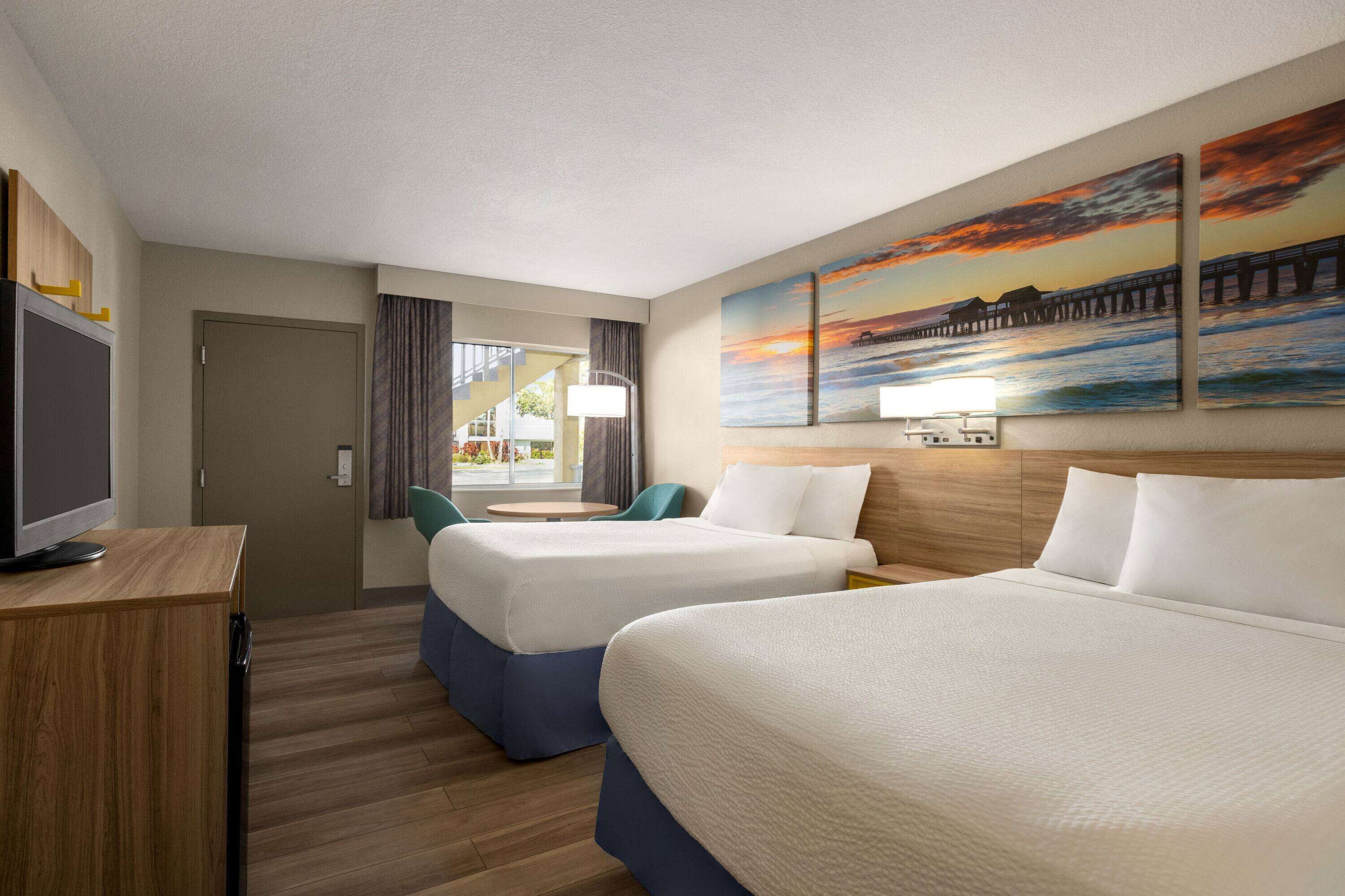A hotel room with two beds, a desk, and a window with curtains.