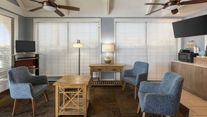 A hotel room with a wooden table, two blue armchairs, a lamp, a TV, and a ceiling fan. - Days Inn by Wyndham Cocoa Beach Port Canaveral (Cocoa Beach)