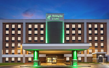 A Holiday Inn & Suites building with a modern design, featuring a prominent entrance with a green-lit canopy and a clear sign above the entrance.