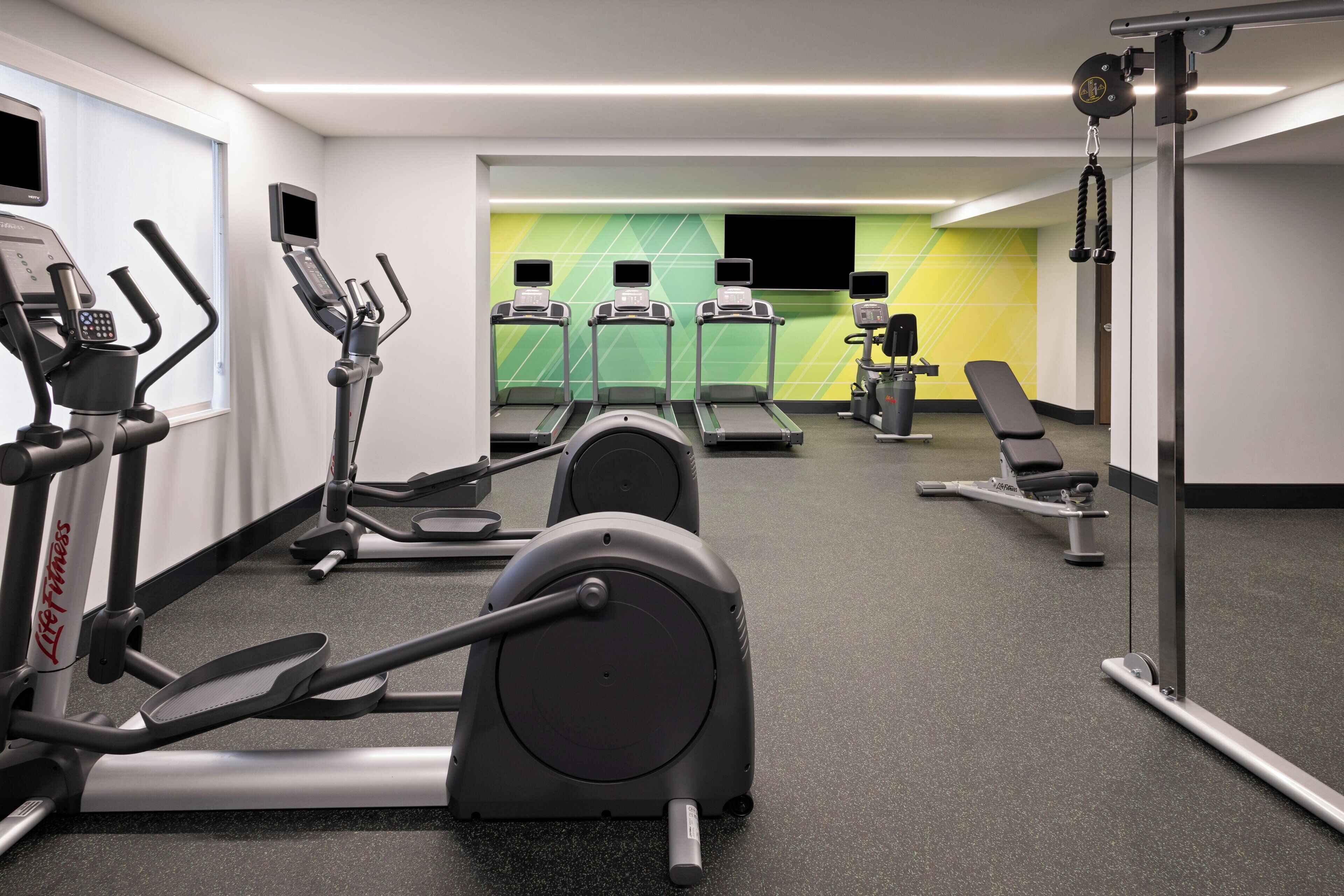 A gym with cardio machines, weightlifting equipment, and a bench.