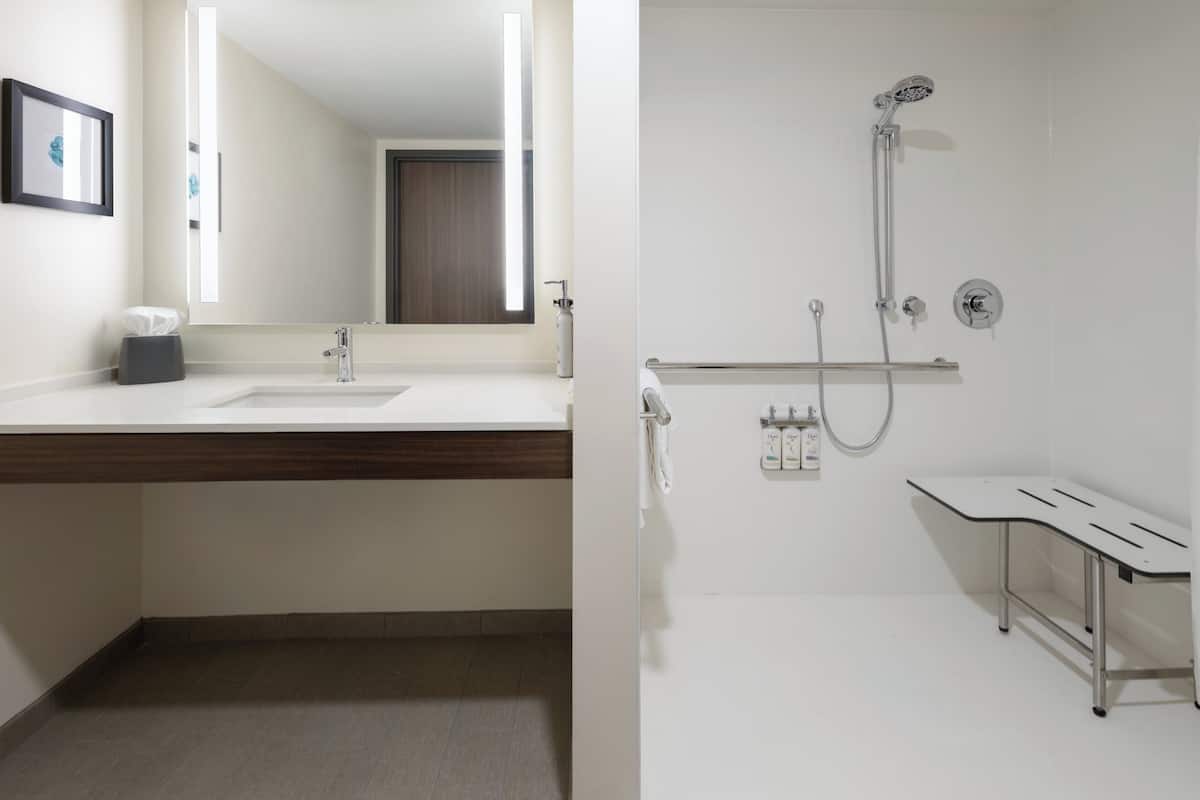 A modern bathroom with a large mirror, a sink, a shower, and a bench.