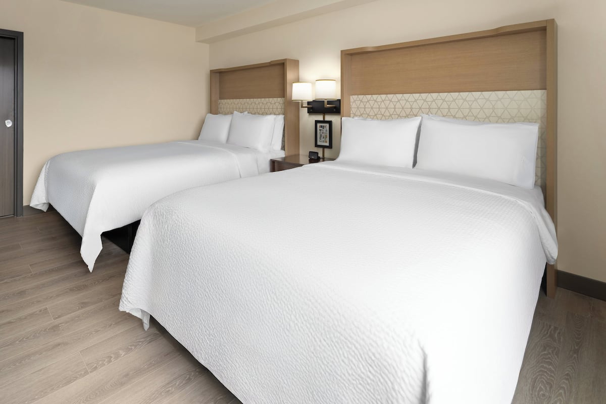 A hotel room with two beds, wooden headboards, a nightstand with a lamp, and a framed picture on the wall.