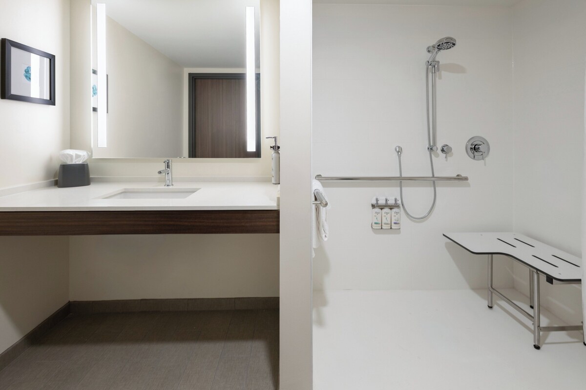 Un bagno moderno con uno specchio grande, un lavabo, una doccia e una panca.
