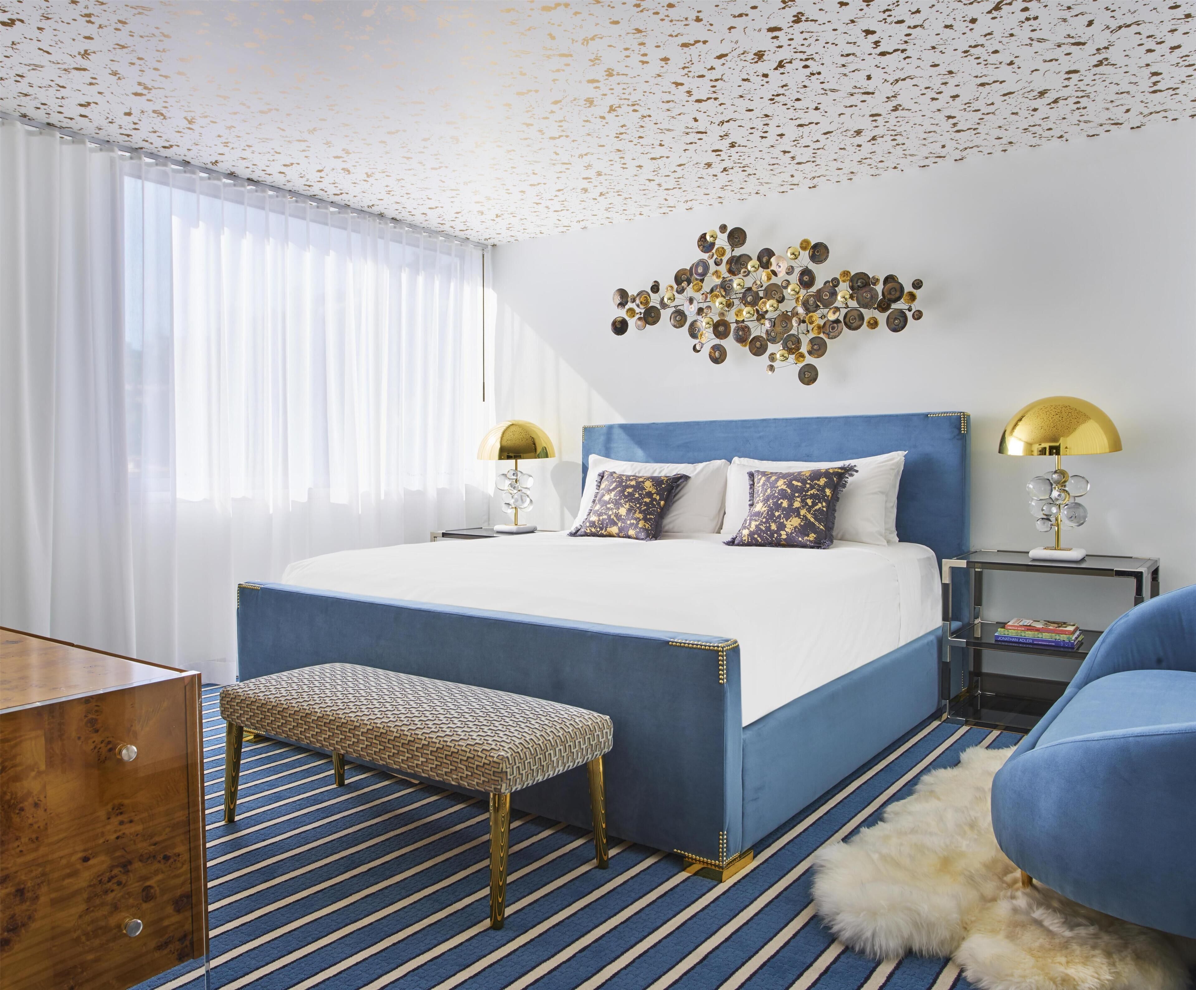 Une chambre d’hôtel moderne avec un grand lit, deux lampes de chevet, un banc et un élément décoratif mural.