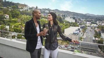 A couple on a balcony overlooking a cityscape with buildings and hills.