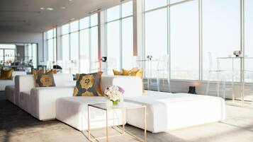 A modern living room with a white sectional sofa, a glass coffee table, and a view of the city through large windows.