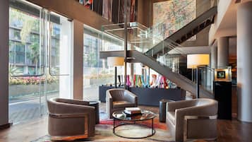 A modern lobby with a staircase, leather seating, a coffee table, and a view of the street.