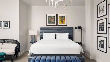 Una habitación de hotel moderna con una cama grande, un banco, un sofá y una araña.