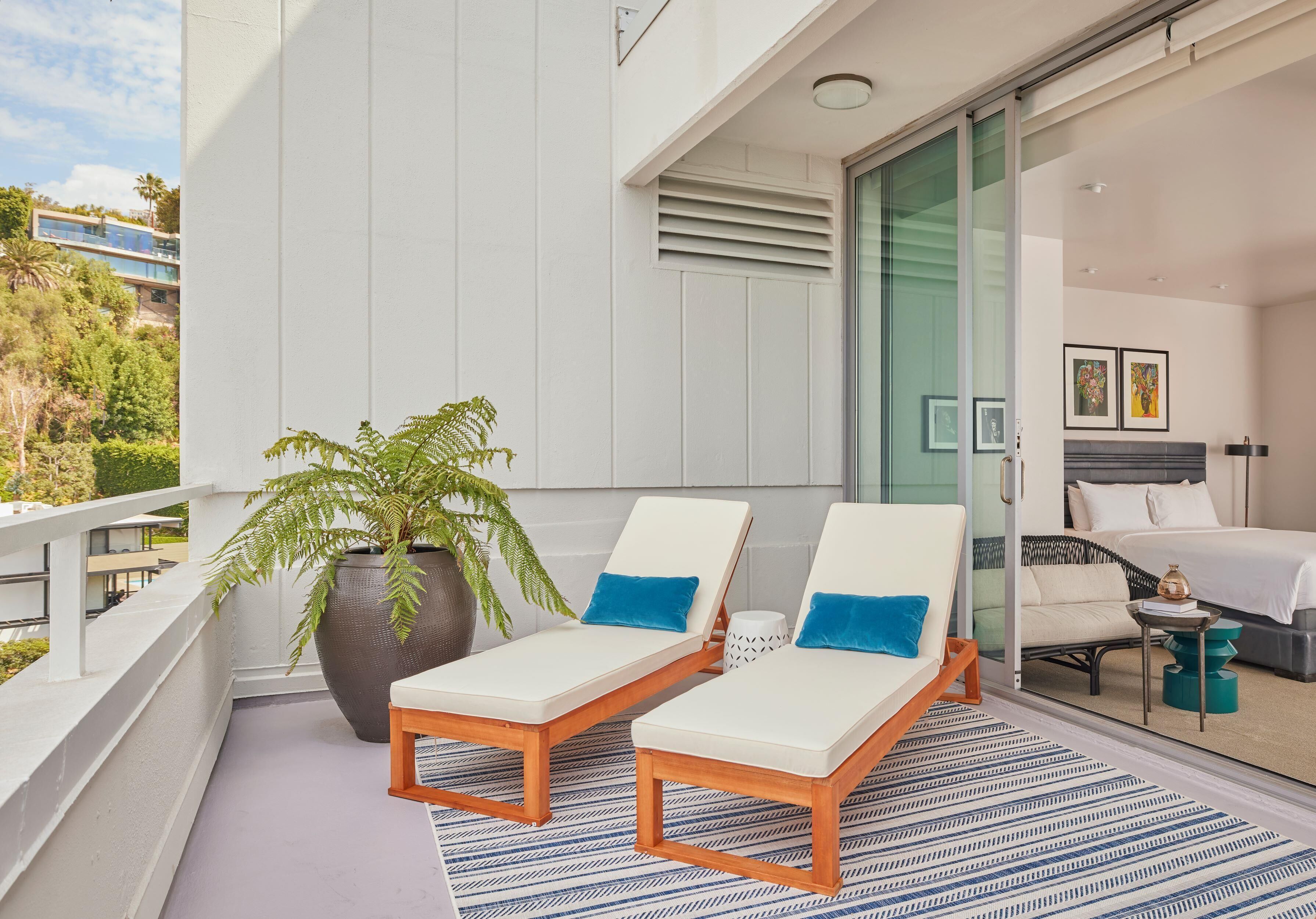 Een balkon met twee loungestoelen, een bloempot en uitzicht op een modern gebouw.