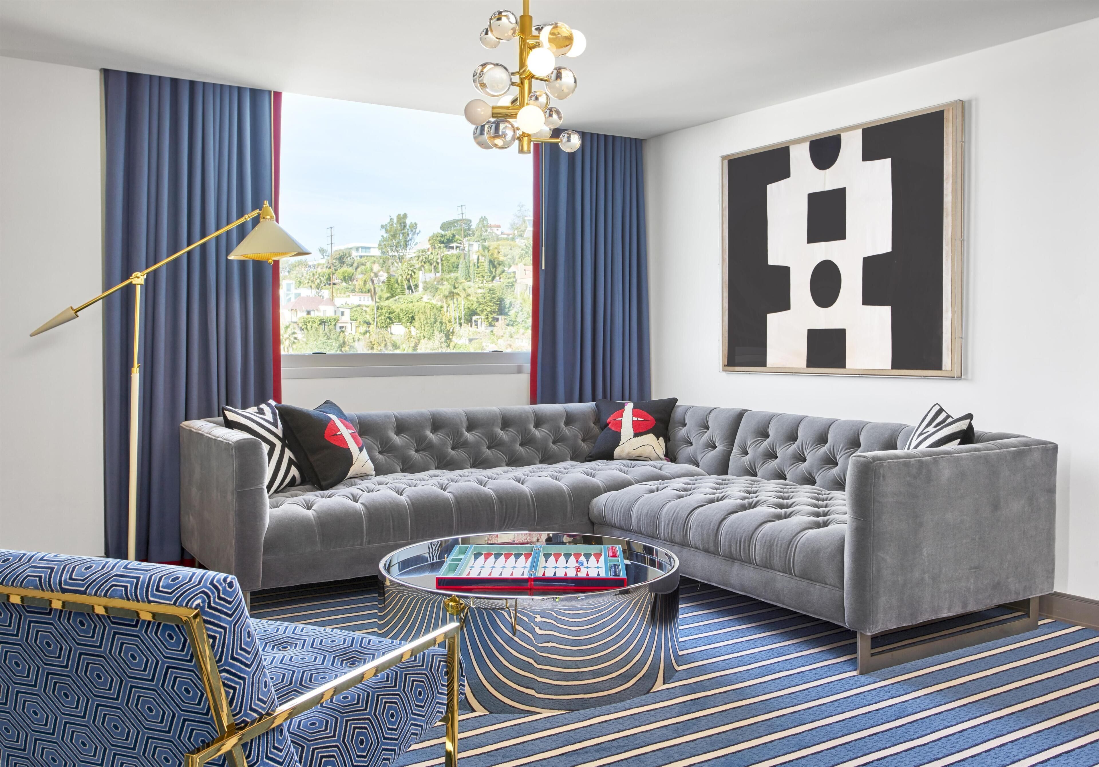 Un salon moderne avec un canapé d’angle, une table basse et une grande fenêtre agrémentée de rideaux.
