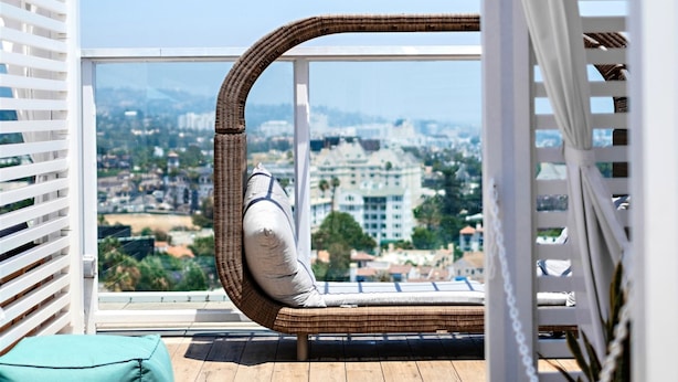A balcony with a wicker chair, a teal cushion, and a potted plant.