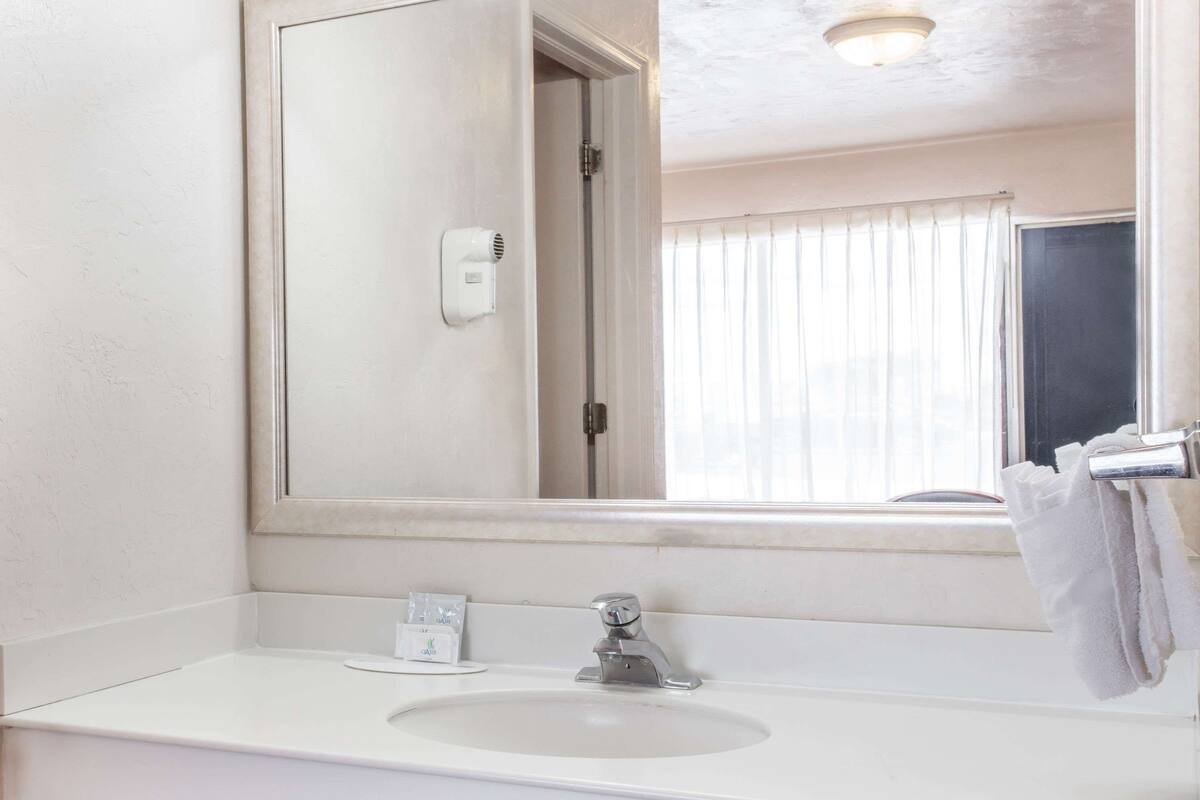 Un baño con lavamanos blanco, un espejo, toallero y una ventana con persianas.
