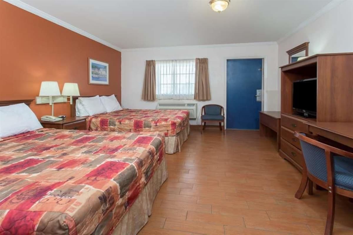 A hotel room with two beds, a desk, a chair, a television, and a window with curtains.